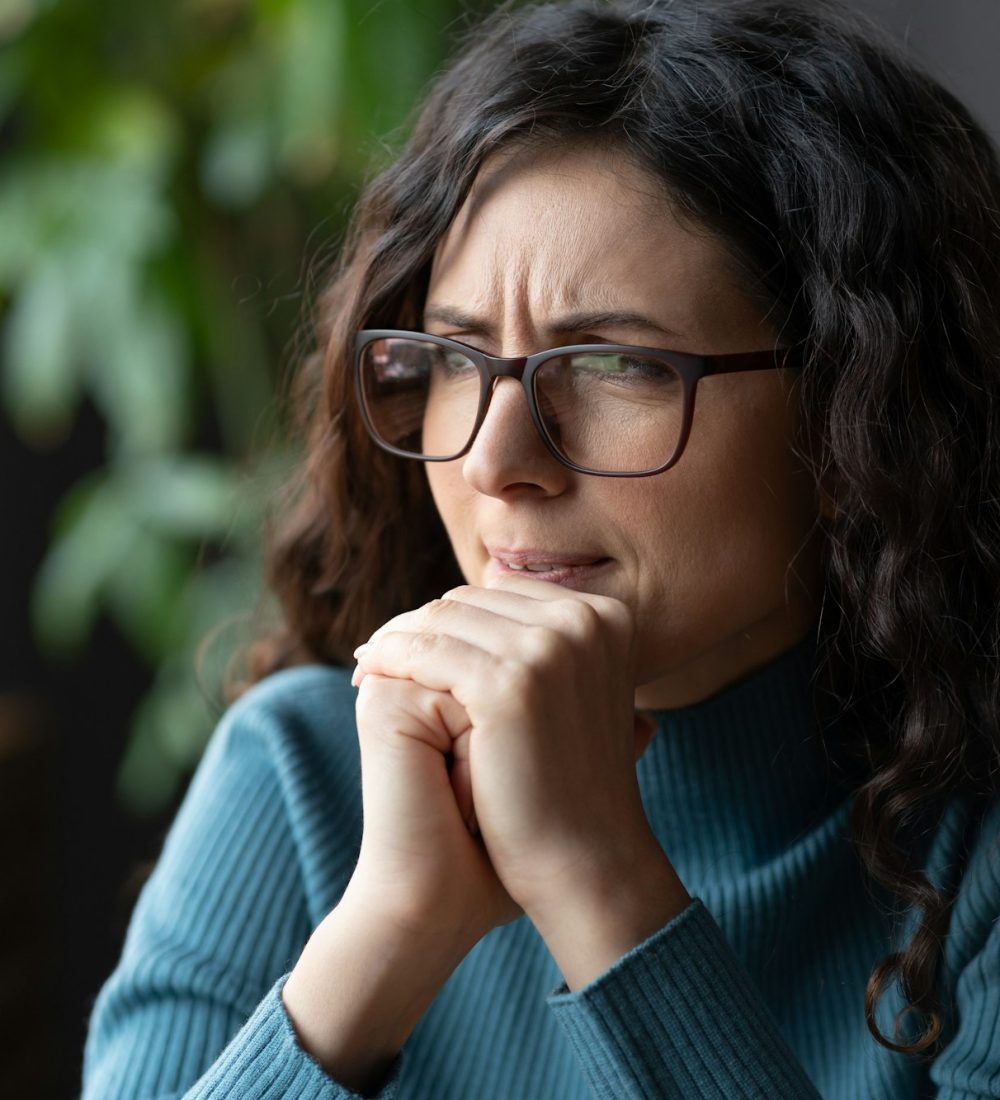 Young worried female employee in glasses feeling anxious, irritable or depressed at workplace